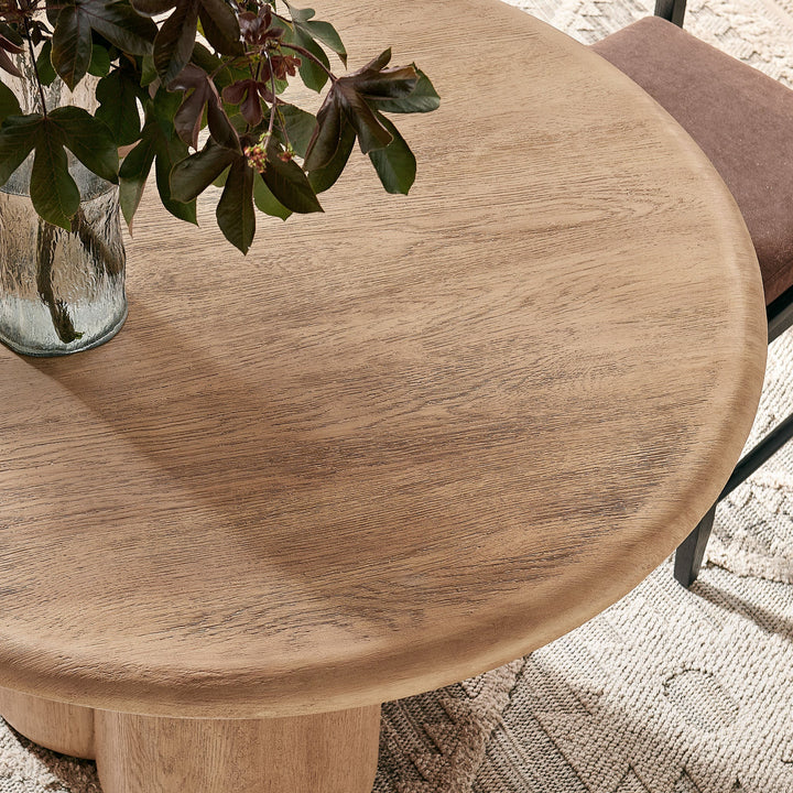 Round wooden table with a vase of leaves on a textured surface